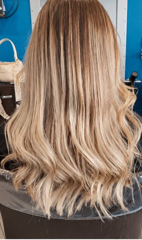 Cheveux longs blond balayé et ondulé, vus de dos, après une coloration en balayage.