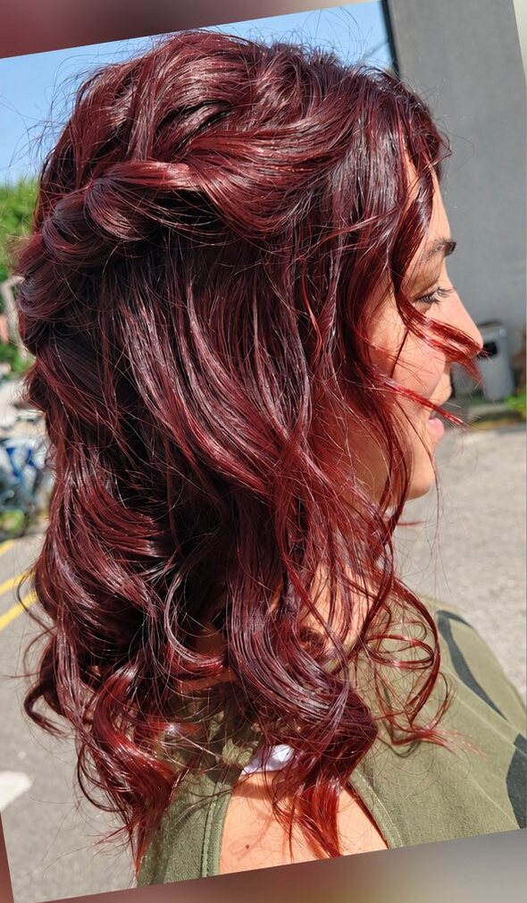 Vue de profil de cheveux mi-longs bouclés rouge bordeaux avec une tresse sur le côté, prise dehors en pleine lumière.