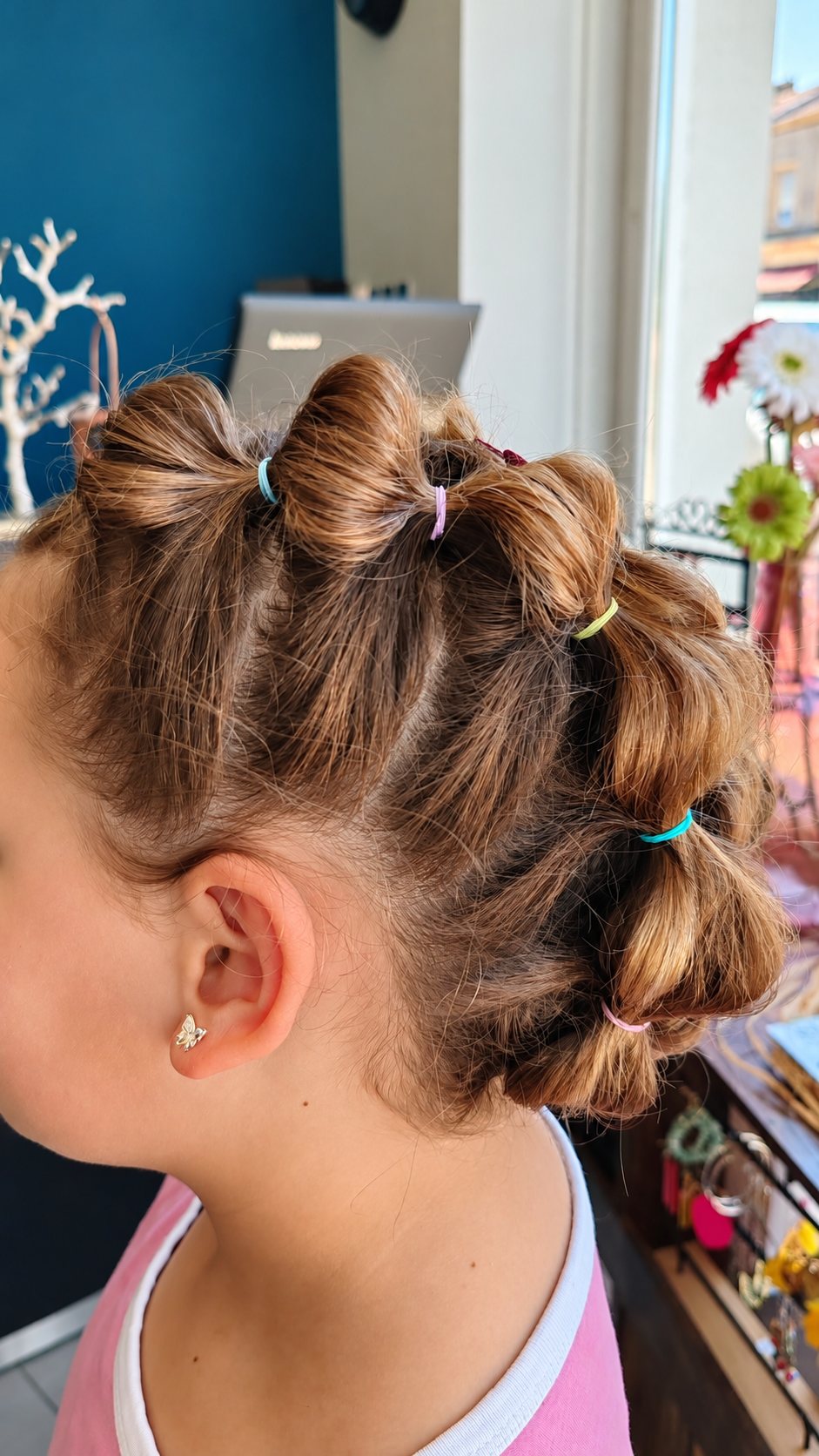 Vue de profil d'une jeune fille portant une coiffure en bulles retenues par de petits élastiques colorés, dans un salon de coiffure lumineux.