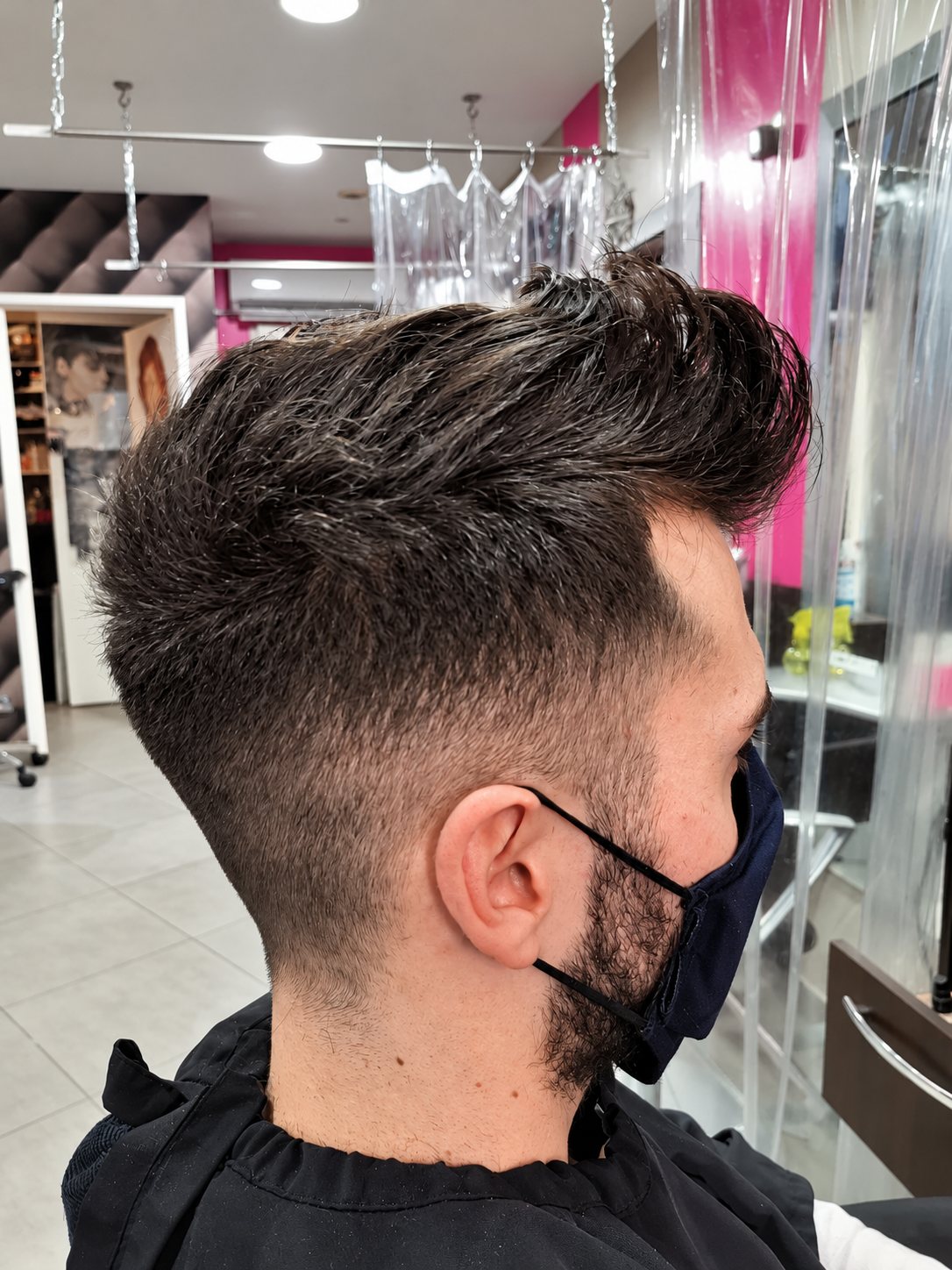 Vue de profil d'un client masqué portant une coupe dégradée avec le dessus texturé, assis dans un salon de coiffure.