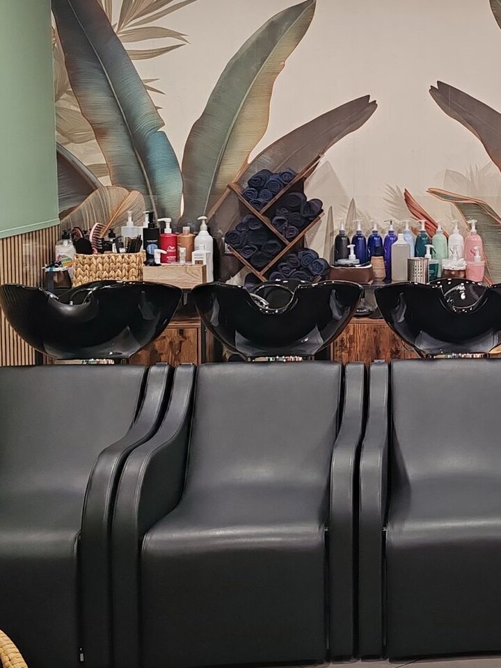 Les bacs de lavage du salon et l'étagère de produits capillaires devant la fresque de feuilles.
